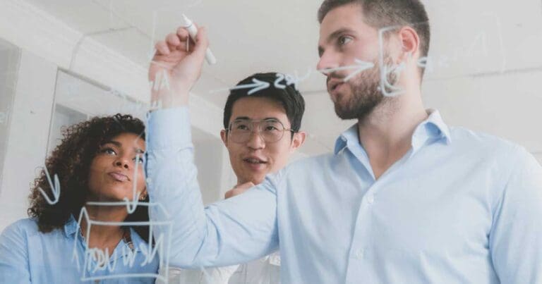 Man-writing-on-clear-board-with-two-people-around-him