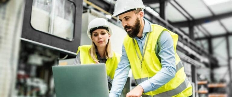 A portrait of an industrial man and woman engineer with laptop in a factory, working.