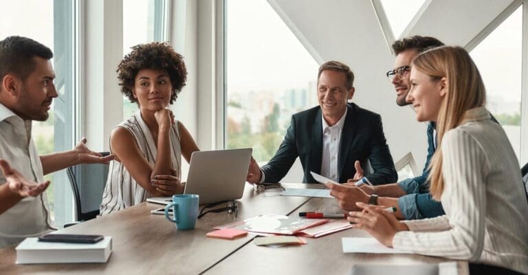 Group of young business people discussing something and smiling while sitting at the office table