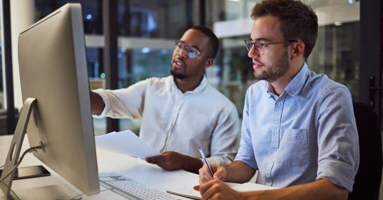 Two coworkers talking about something on computer screen in office