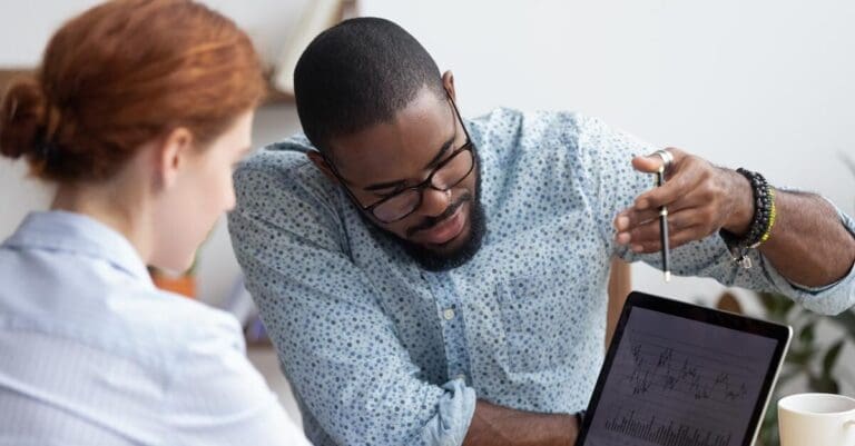 Two colleagues in office reviewing data on computer screen