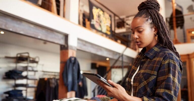 Female Owner Of Fashion Store Using Digital Tablet To Check Stock In Clothing Store