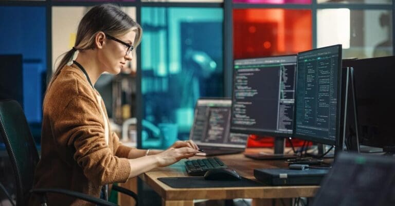 Young Woman Programming On Desktop Computer With Two Monitors Setup in Spacious Office.