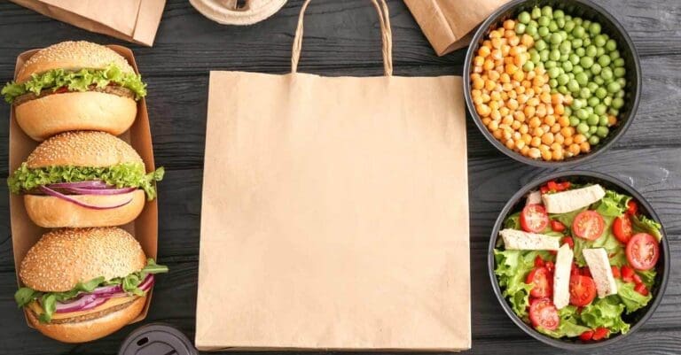 Food, including hamburgers and salad, next to delivery bag. Food industry