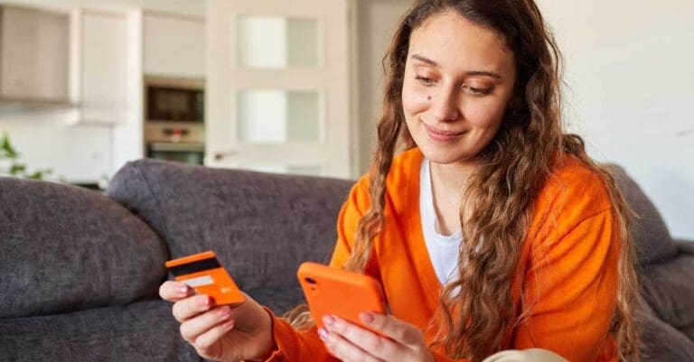 Woman dressed in orange colors shopping with her smartphone from the sofa