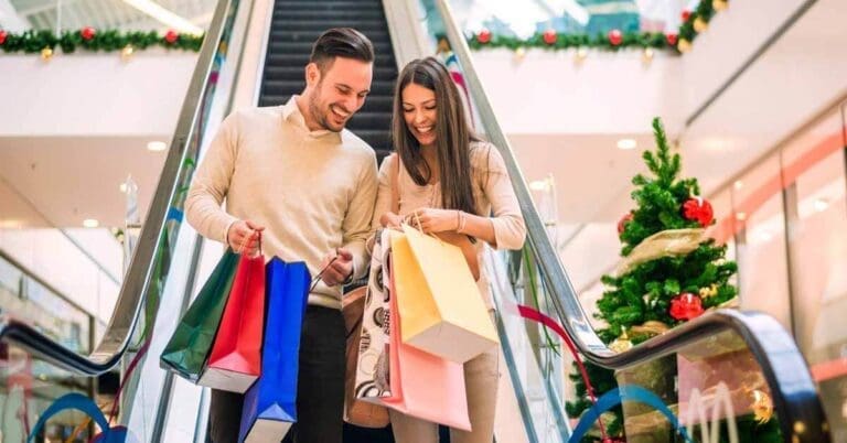 Man and woman in shopping mall, holding shopping bags near Christmas decor, doing holiday shopping