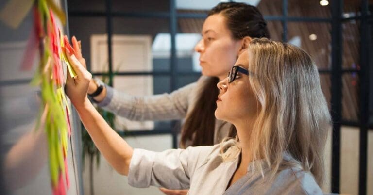 Two business women in the office putting post-it notes on white board. Agile methodology, project management, MVP