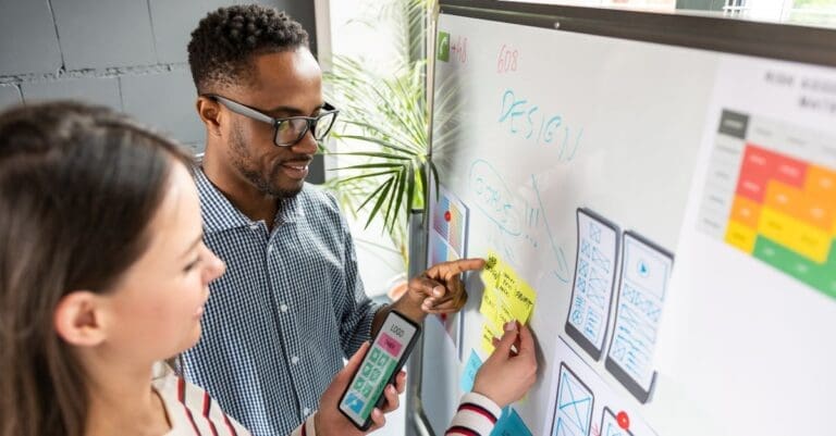 Designers standing at white board planning mobile app UX