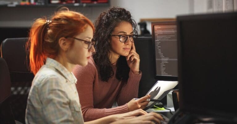 Two programmers looking at code on computer monitors in office