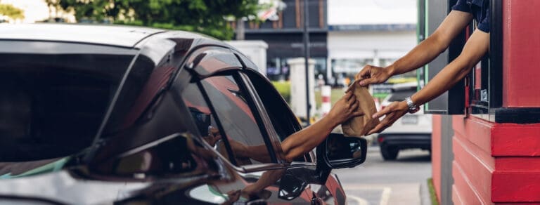 Hand Man in car receiving coffee in drive thru fast food restaurant. Staff serving takeaway order for driver in delivery window. Drive through and takeaway for buy fast food for